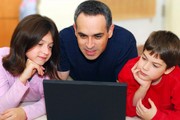 A father with a son and daughter look at a laptop computer.